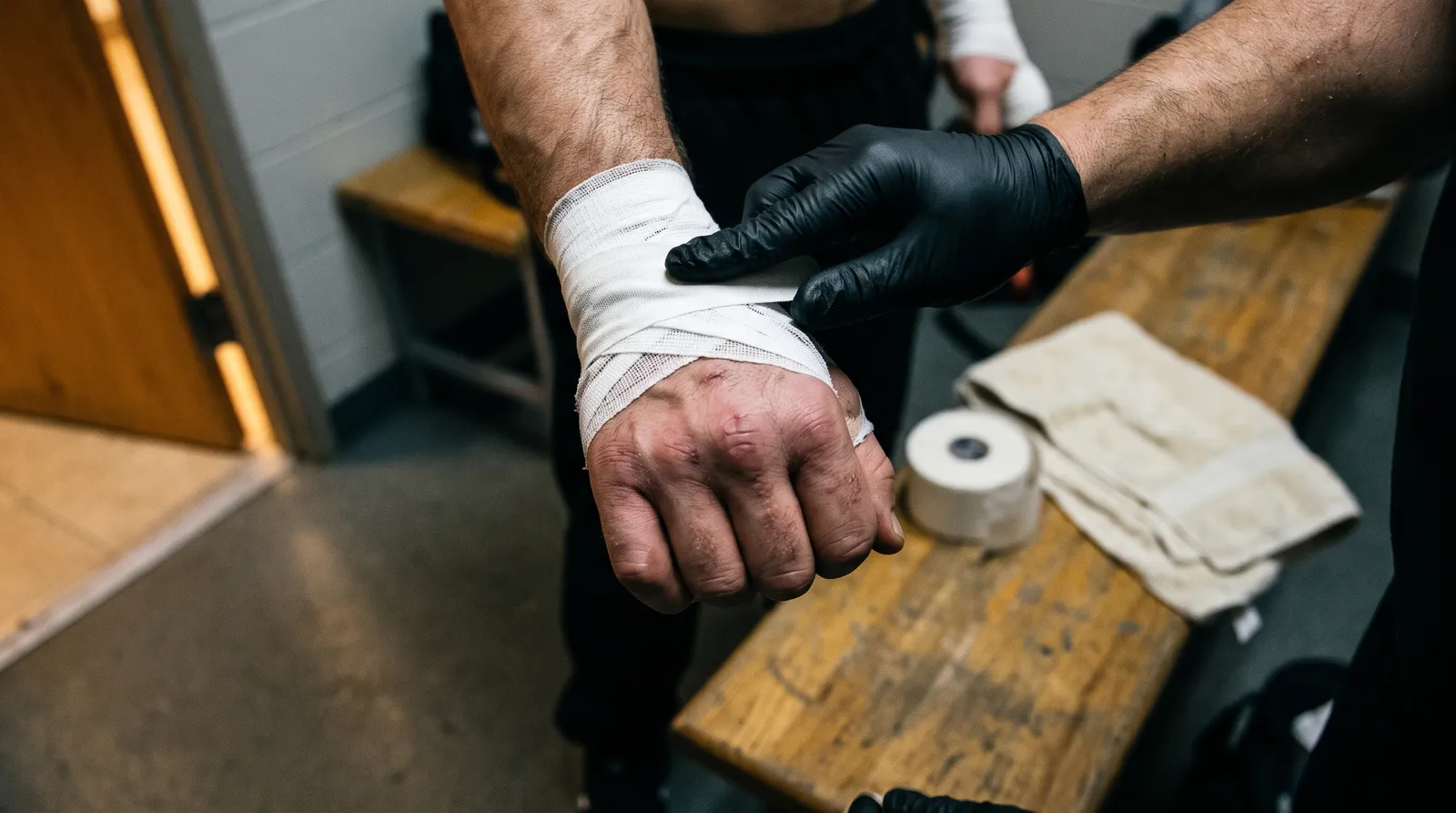 A fighter's scarred hands being taped in a locker room before a bout