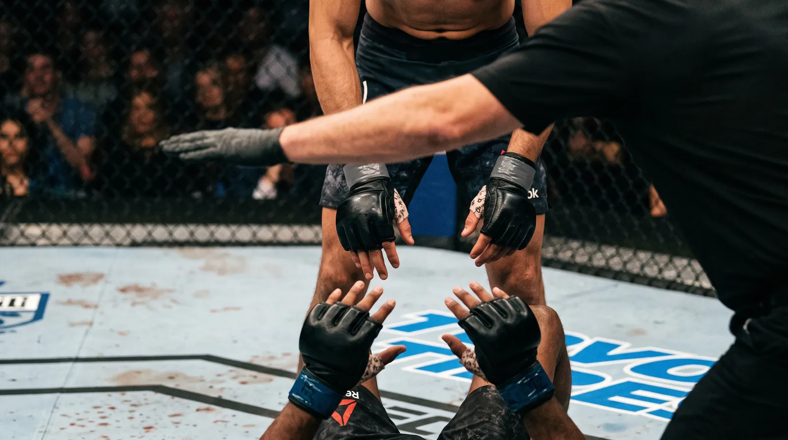 A referee's arm reaches between two fighters' gloves on the canvas as a fight is stopped