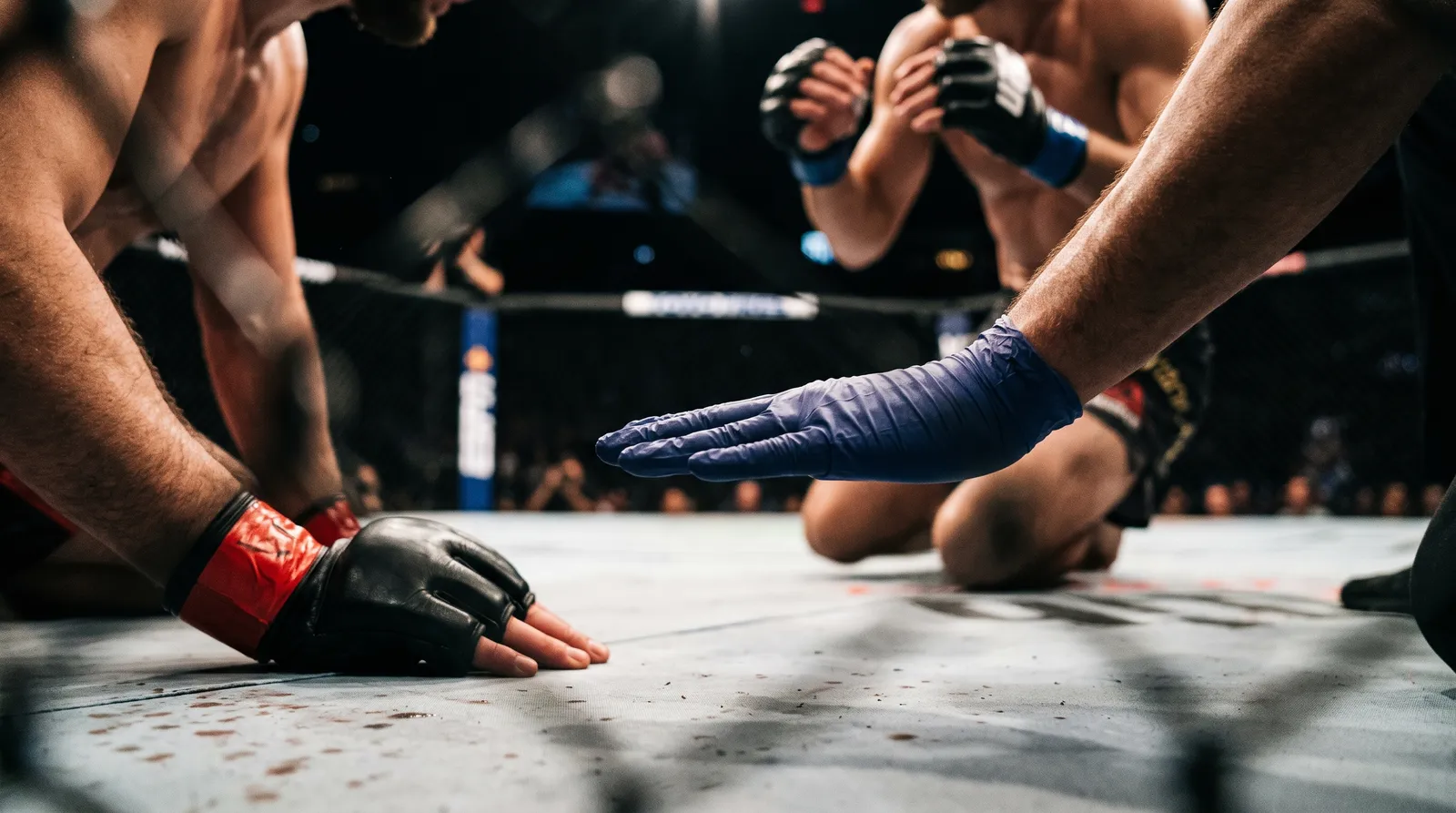 A referee's hand separates two fighters as one braces on the canvas